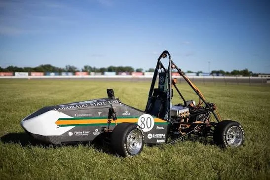 A Colorado State University Formula SAE race car, number 80, parked on the grass at a racetrack